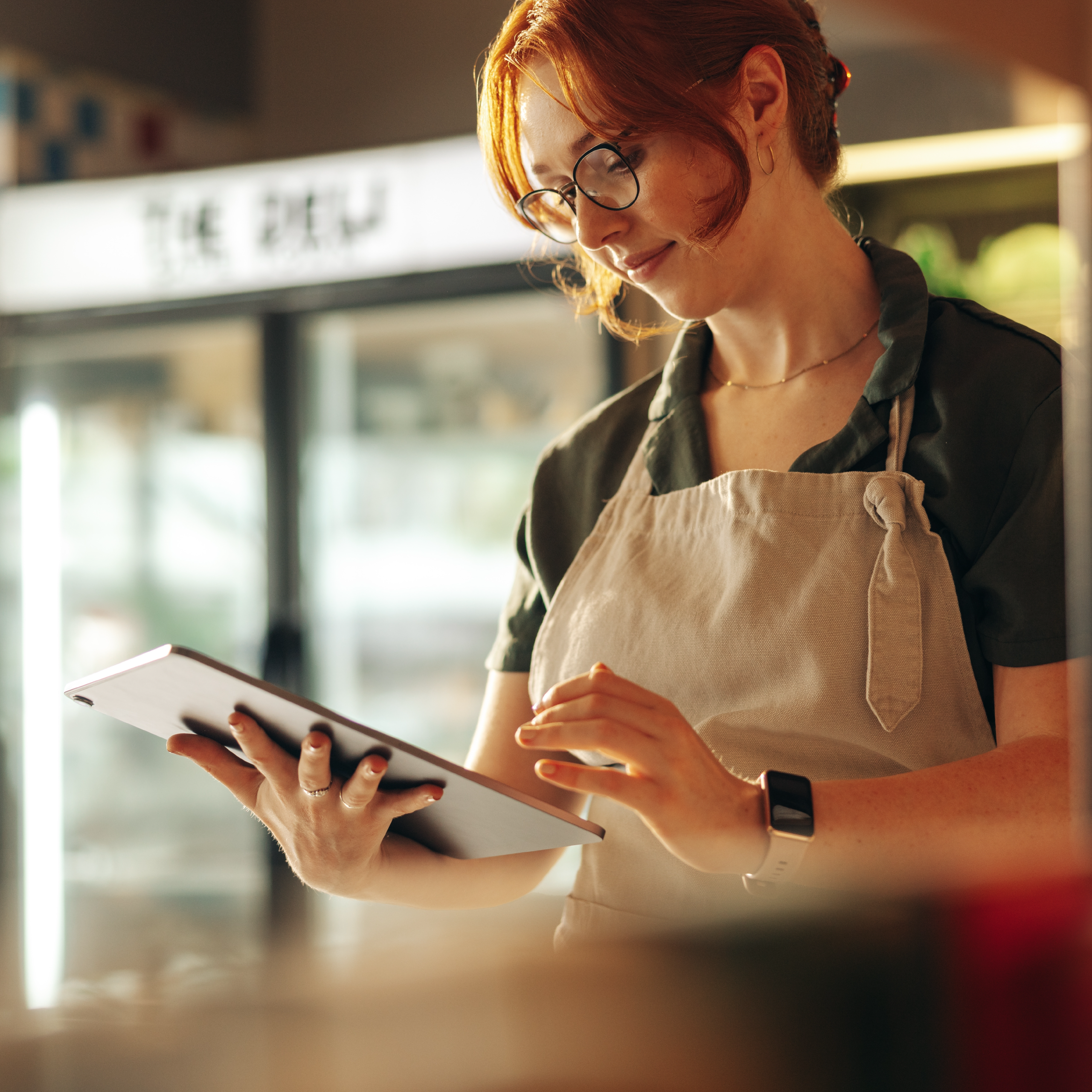 Woman wearing an apron holding an iPad in a cafe