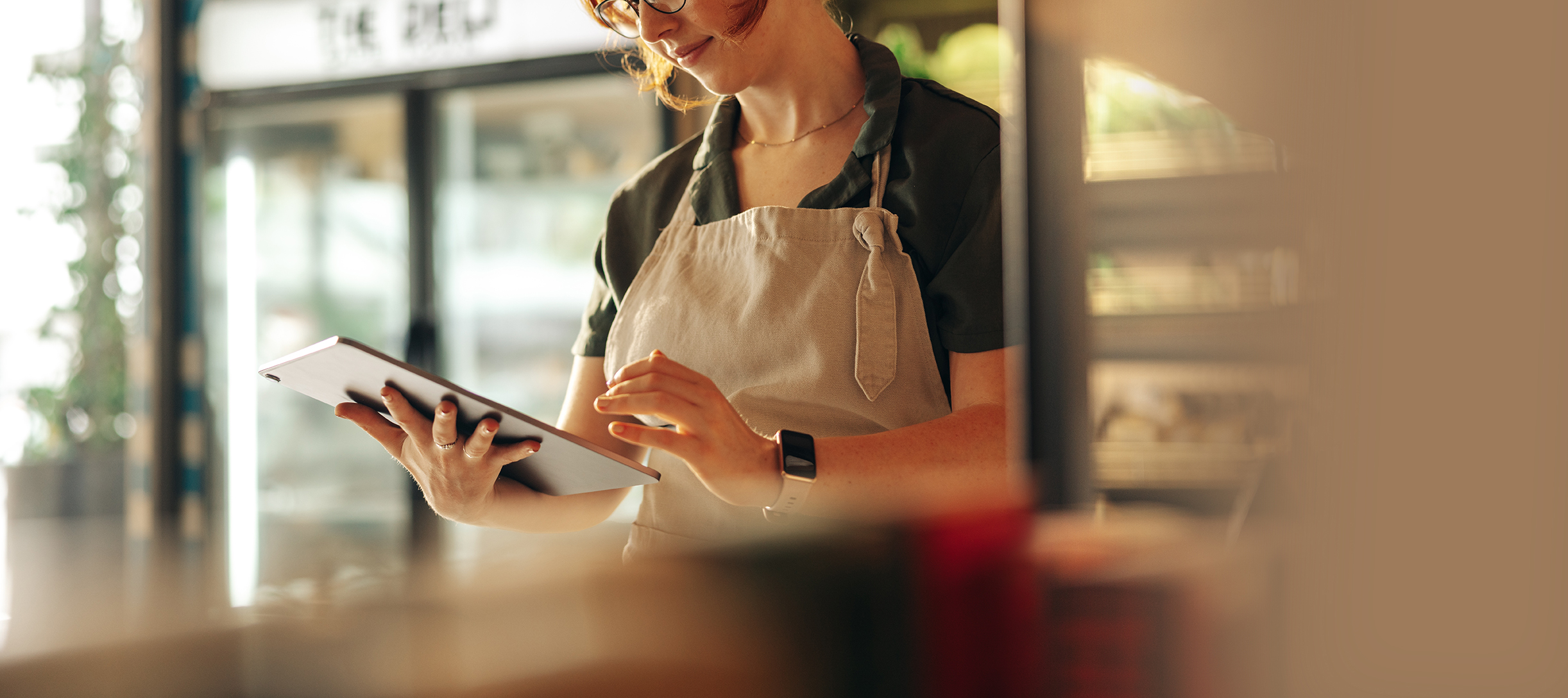 Cheerful shop owner using a digital tablet while standing in her cafe